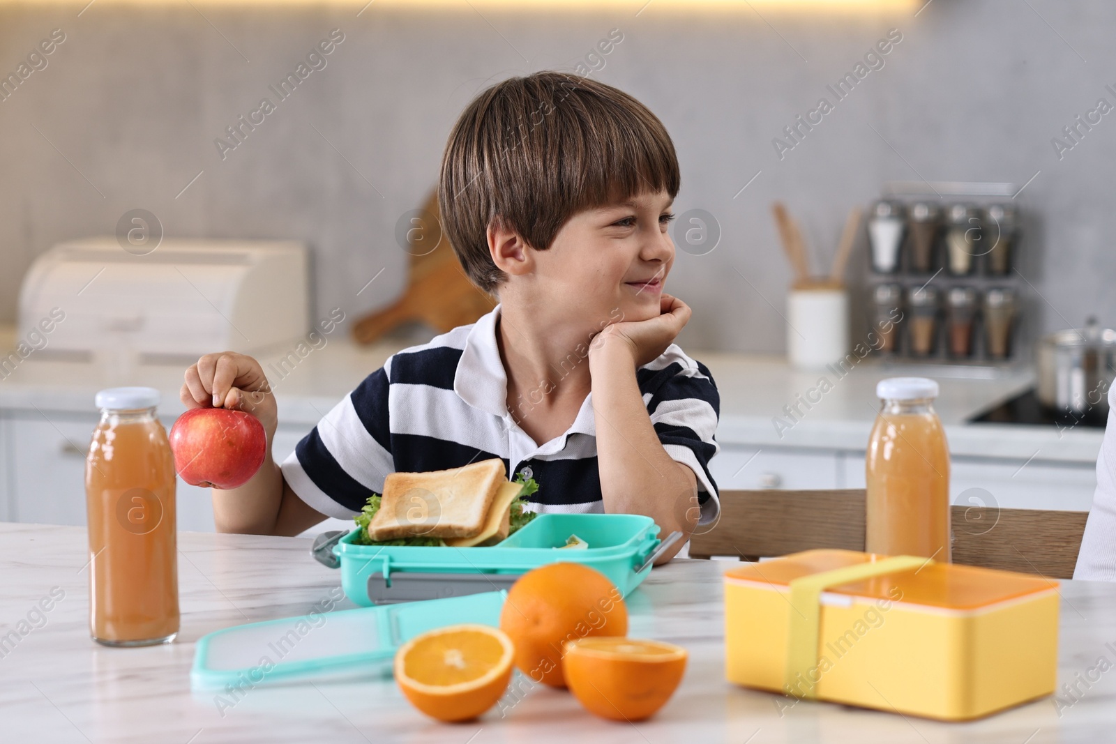 Photo of Cute boy preparing school lunch boxes with healthy food at white marble table in kitchen