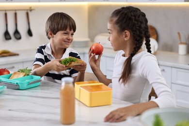 Photo of Cute children preparing school lunch boxes with healthy food at white marble table in kitchen