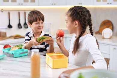 Cute children preparing school lunch boxes with healthy food at white marble table in kitchen