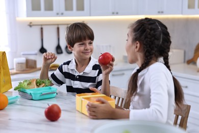 Cute children preparing school lunch boxes with healthy food at white marble table in kitchen