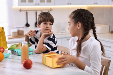 Photo of Cute children preparing school lunch boxes with healthy food at white marble table in kitchen