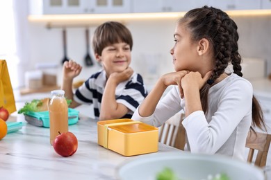 Photo of Cute children preparing school lunch boxes with healthy food at white marble table in kitchen