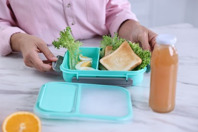 Photo of Woman packing school lunch box with healthy meal at white marble table in kitchen, closeup