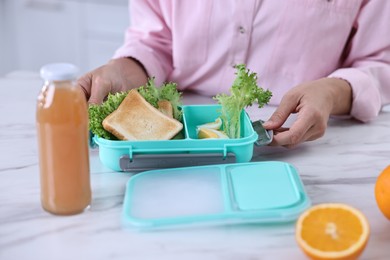 Photo of Woman packing school lunch box with healthy meal at white marble table in kitchen, closeup