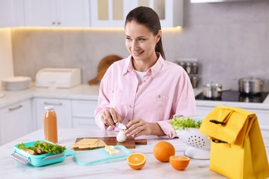 Photo of Smiling woman making snacks for school lunch box at white marble table in kitchen