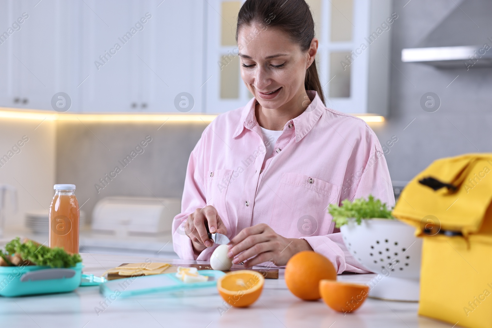 Photo of Smiling woman making snacks for school lunch box at white marble table in kitchen