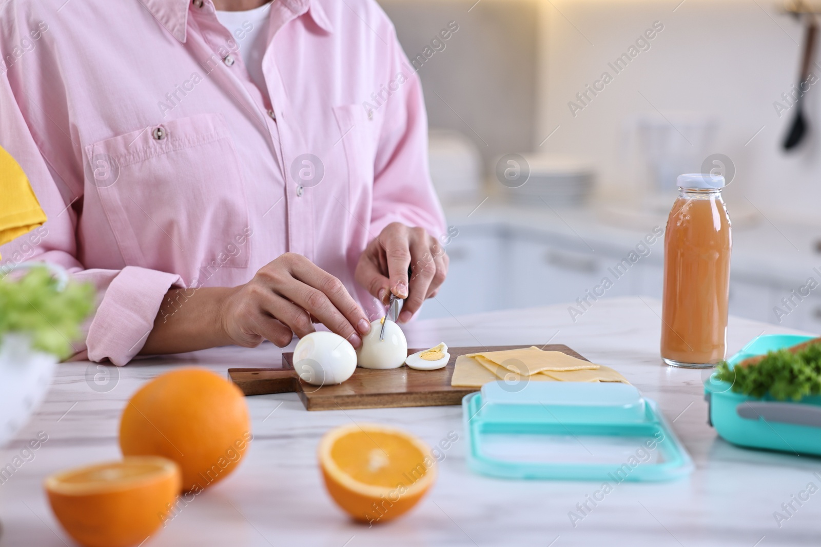 Photo of Woman making snacks for school lunch box at white marble table in kitchen, closeup