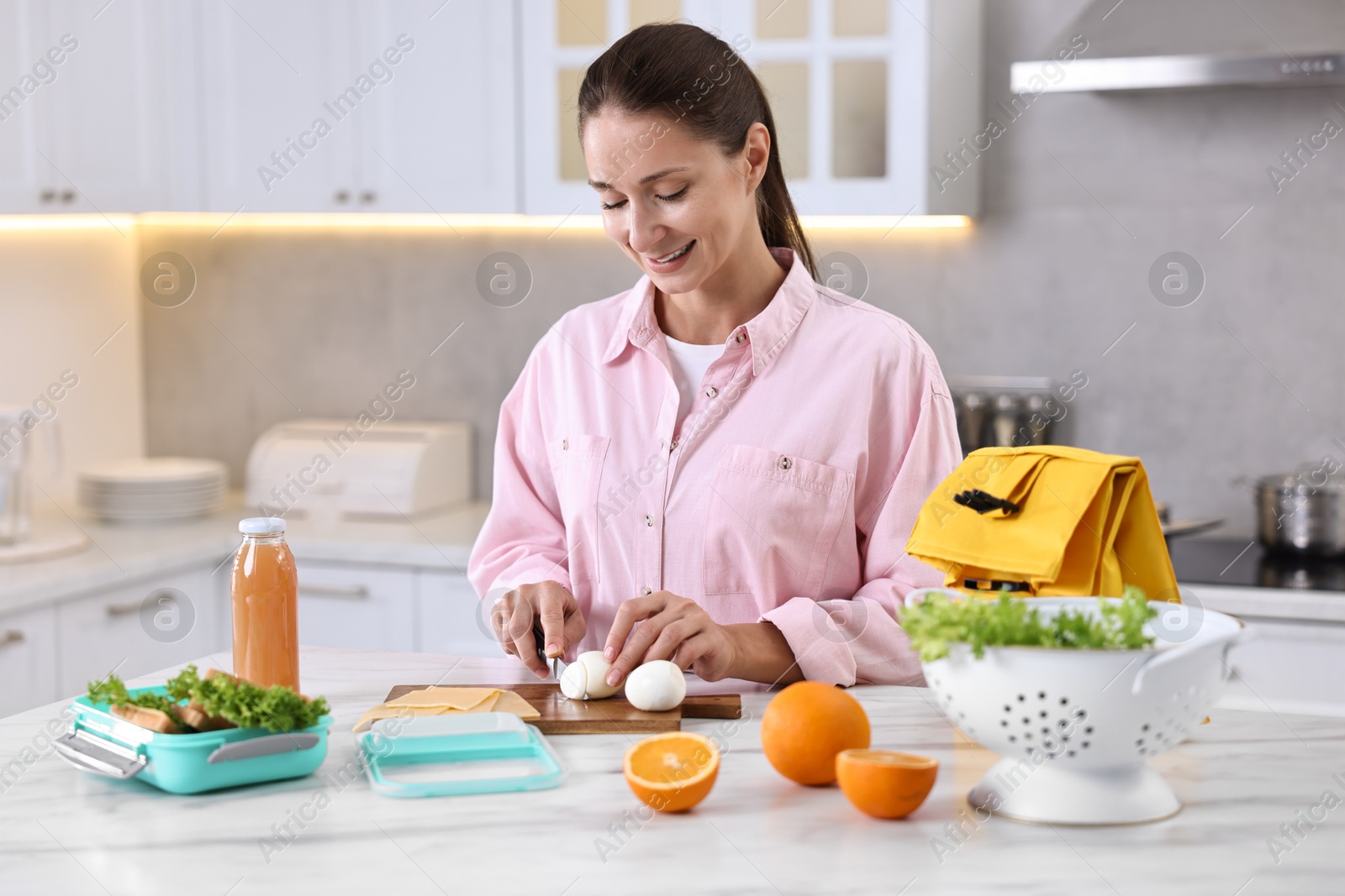 Photo of Smiling woman making snacks for school lunch box at white marble table in kitchen