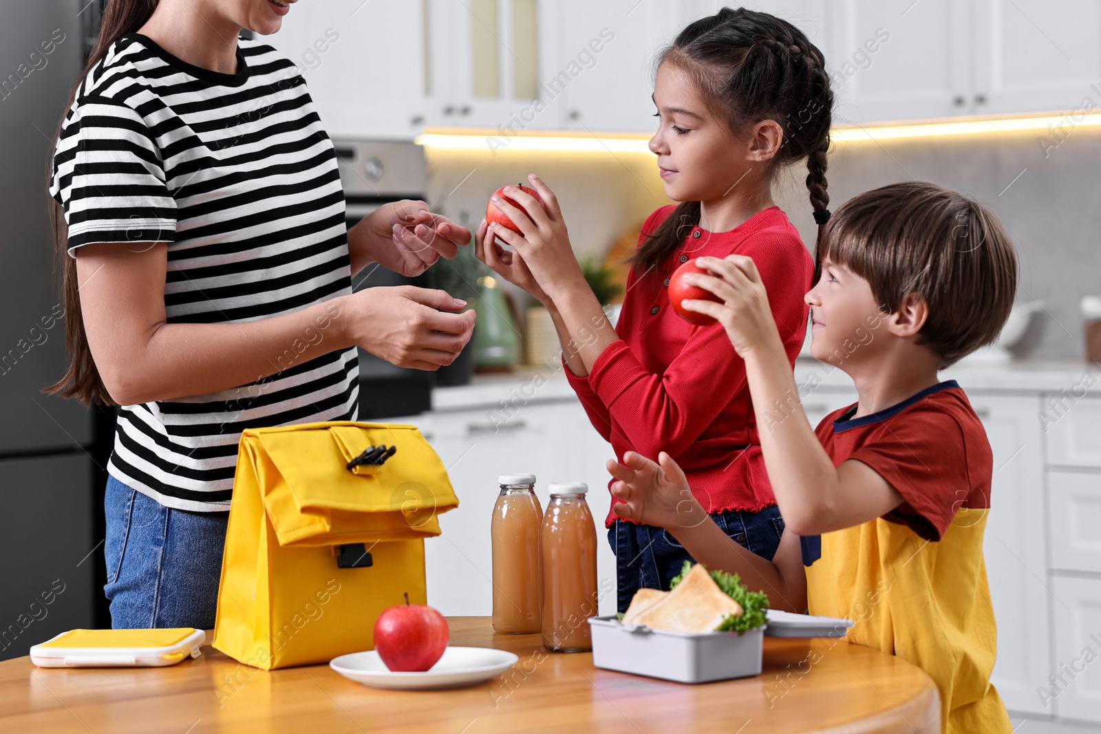 Photo of Mother and her children preparing school lunch box with healthy food at wooden table in kitchen, closeup