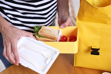 Photo of Woman packing lunch box at wooden table in kitchen, closeup. Preparing for school