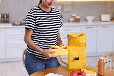 Woman packing lunch box with healthy food at wooden table in kitchen, closeup. Preparing for school