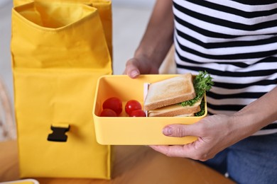 Woman packing lunch box with healthy snacks at wooden table in kitchen, closeup. Preparing for school