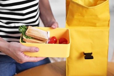 Photo of Woman packing lunch box with healthy snacks at wooden table in kitchen, closeup. Preparing for school