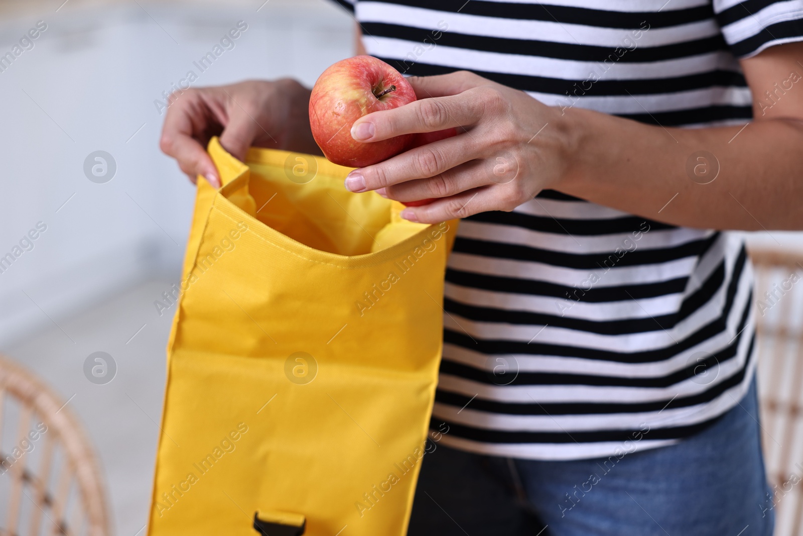 Photo of Woman putting fresh apple into school lunch bag in kitchen, closeup