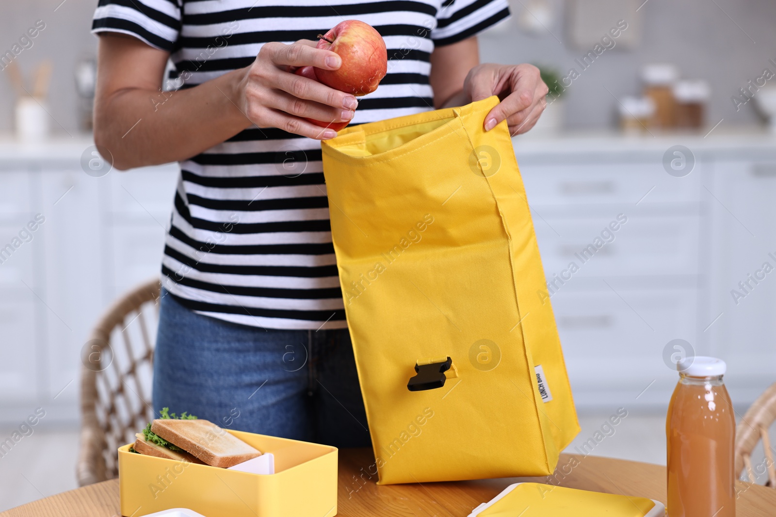 Photo of Woman packing lunch box with healthy food at wooden table in kitchen, closeup. Preparing for school