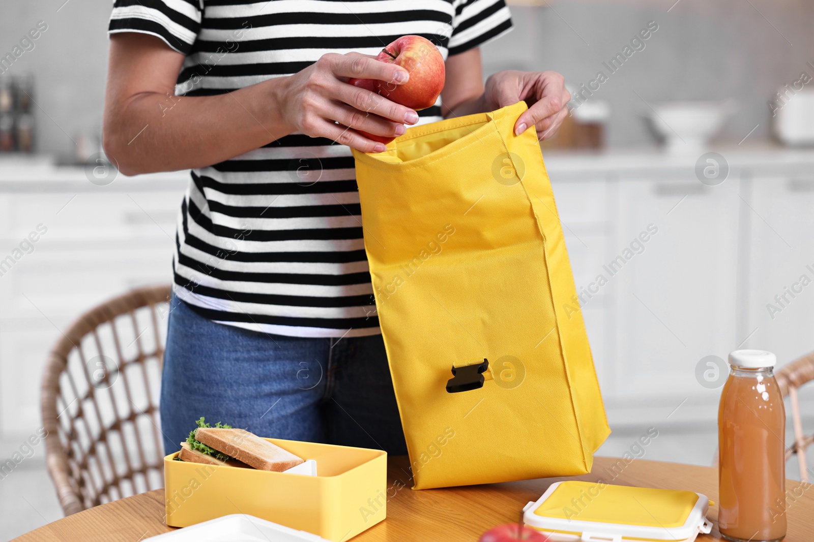 Photo of Woman packing lunch box with healthy food at wooden table in kitchen, closeup. Preparing for school