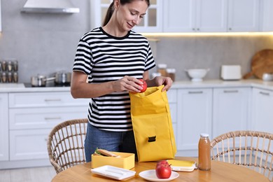 Woman packing school lunch box with healthy food at wooden table in kitchen