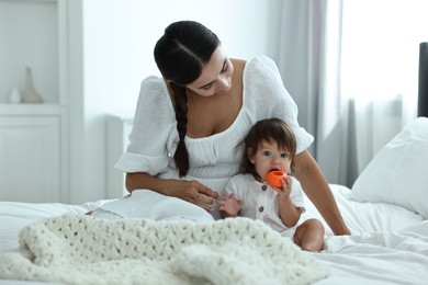 Photo of Beautiful young mother and her cute little baby with toy on bed at home