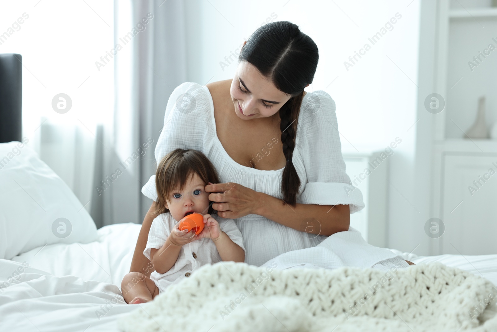 Photo of Beautiful young mother and her cute little baby with toy on bed at home