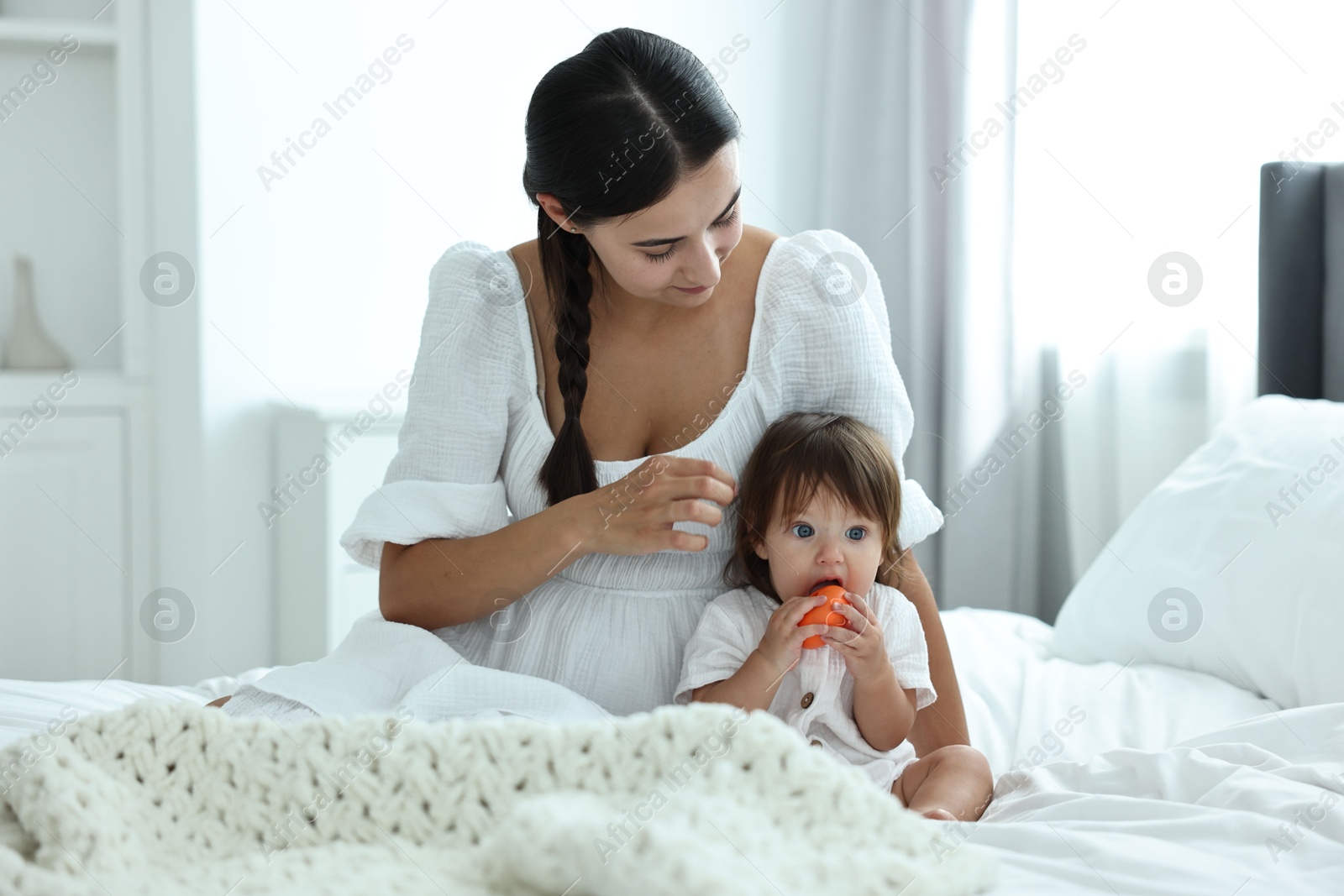 Photo of Beautiful young mother and her cute little baby with toy on bed at home