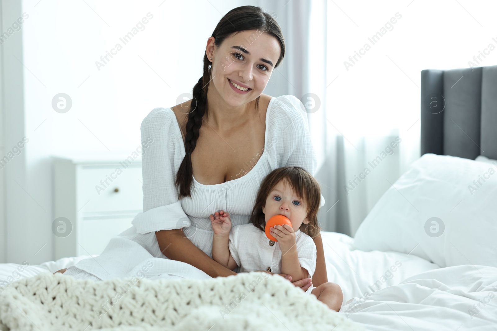 Photo of Beautiful young mother and her cute little baby with toy on bed at home