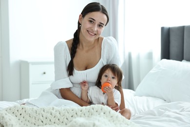 Photo of Beautiful young mother and her cute little baby with toy on bed at home