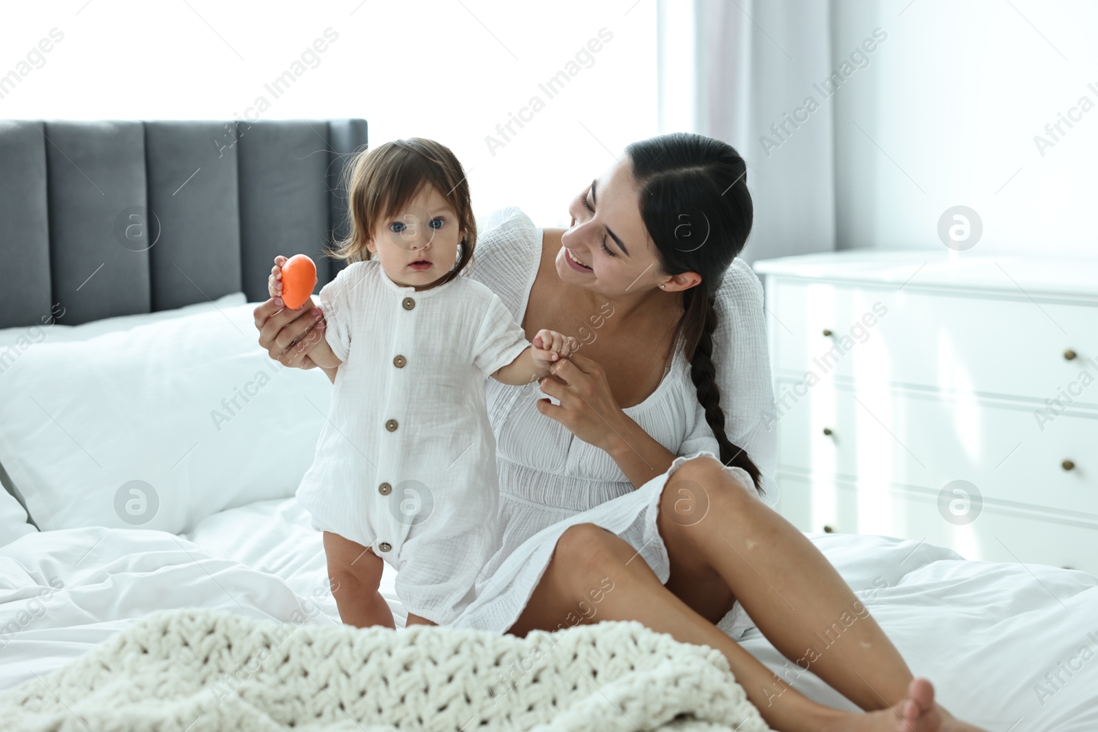 Photo of Beautiful young mother and her cute little baby with toy on bed at home