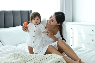 Beautiful young mother and her cute little baby with toy on bed at home