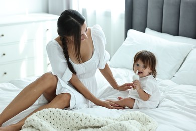 Photo of Beautiful young mother and her cute little baby with rattle on bed at home