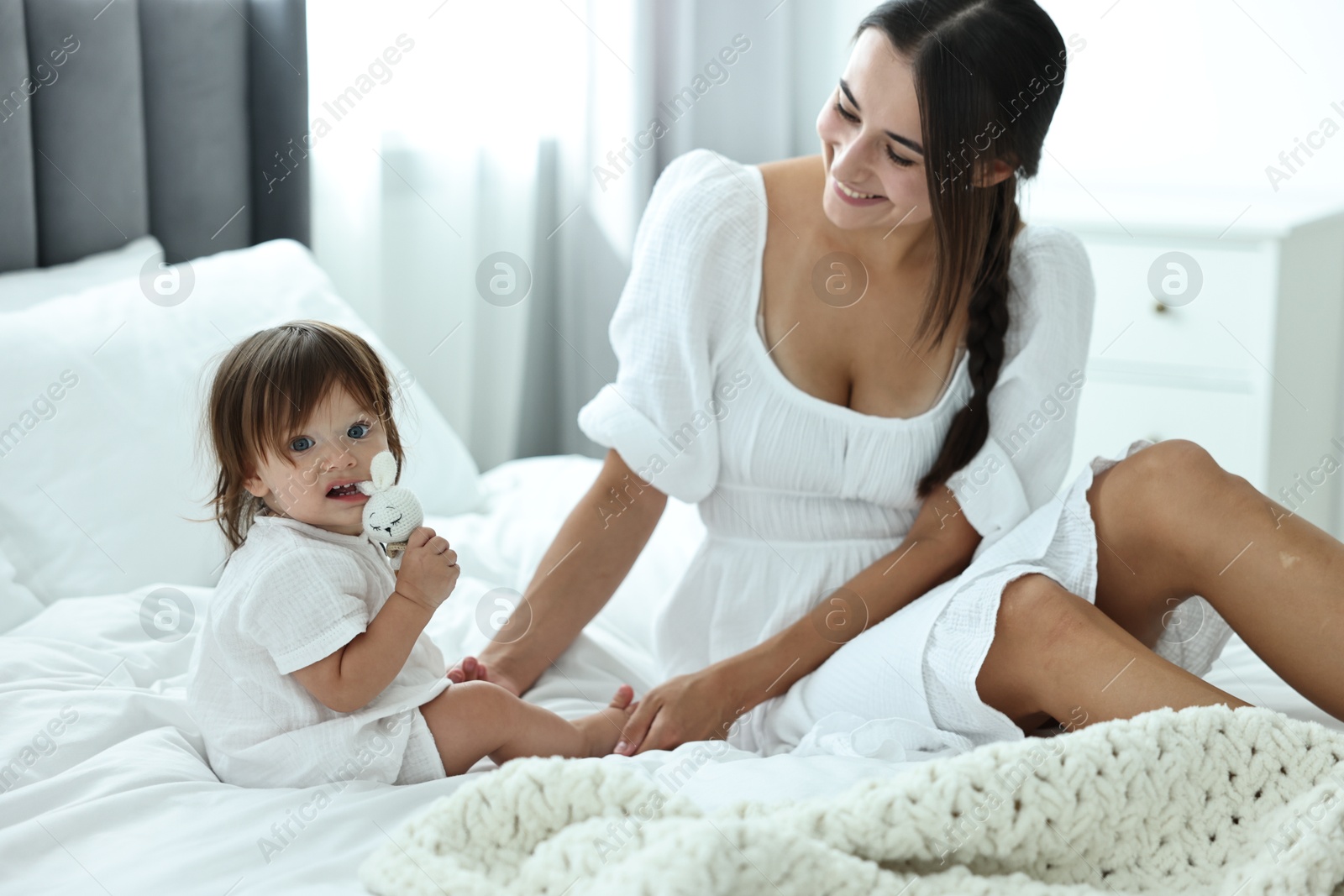 Photo of Beautiful young mother and her cute little baby with rattle on bed at home