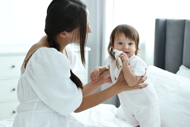 Beautiful young mother and her cute little baby with rattle on bed at home