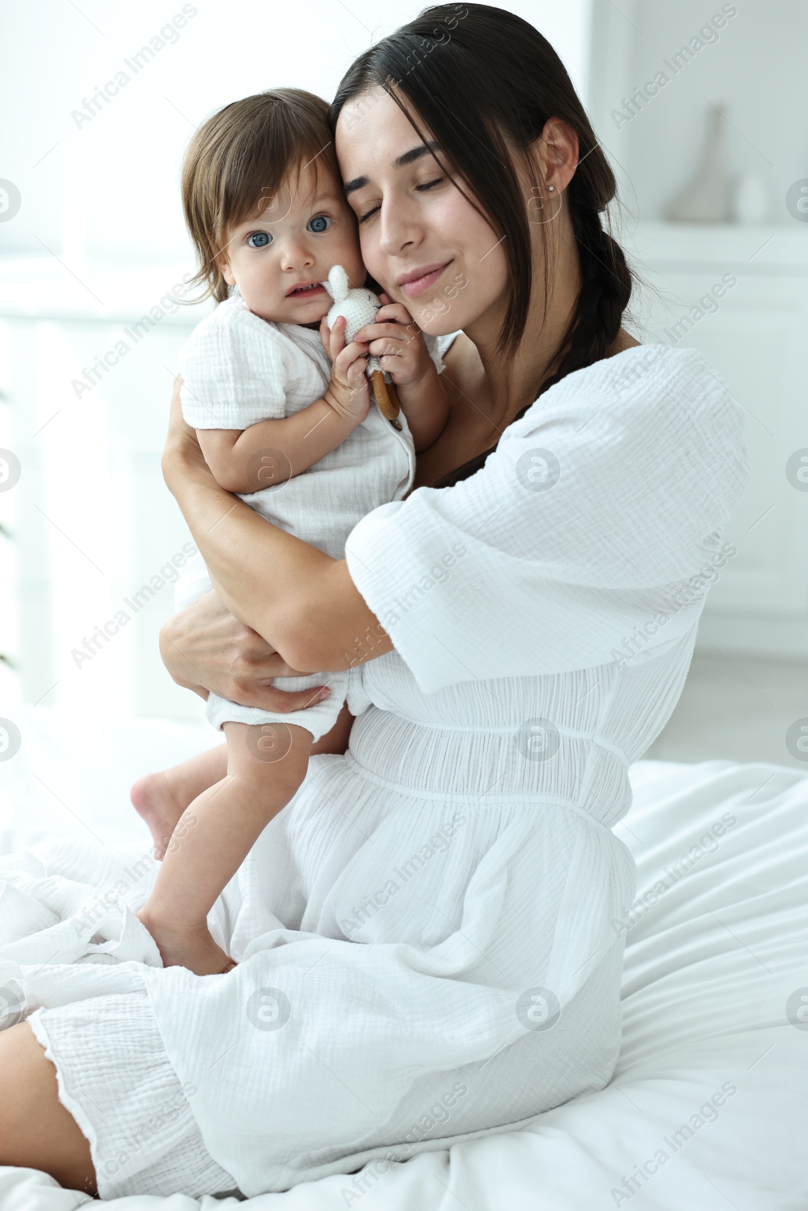 Photo of Beautiful young mother and her cute little baby with rattle on bed at home