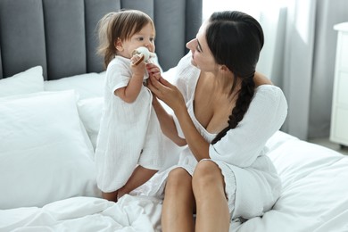 Beautiful young mother and her cute little baby with rattle on bed at home