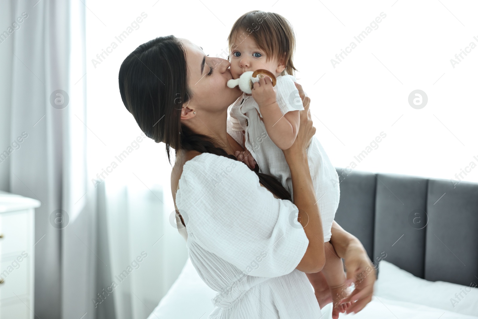 Photo of Beautiful young mother and her cute little baby with rattle in bedroom