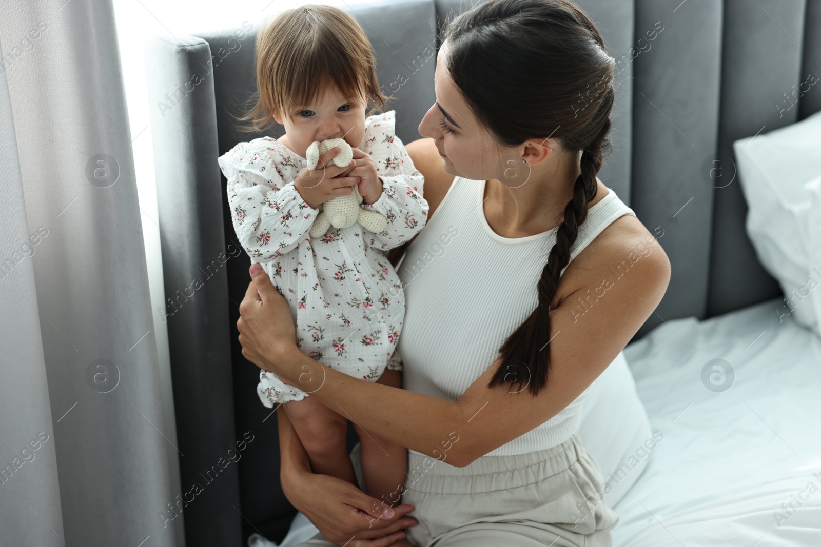 Photo of Beautiful young mother and her cute little baby with rabbit toy on bed at home