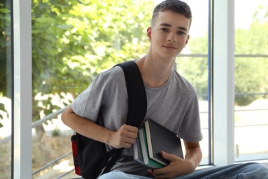 Photo of Portrait of teenage boy with backpack and books indoors