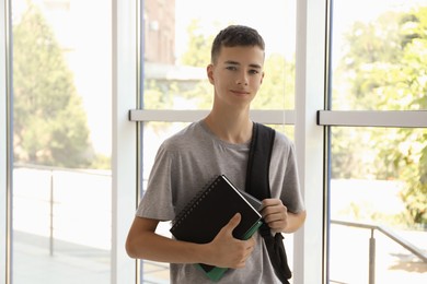 Photo of Portrait of teenage boy with backpack and books indoors