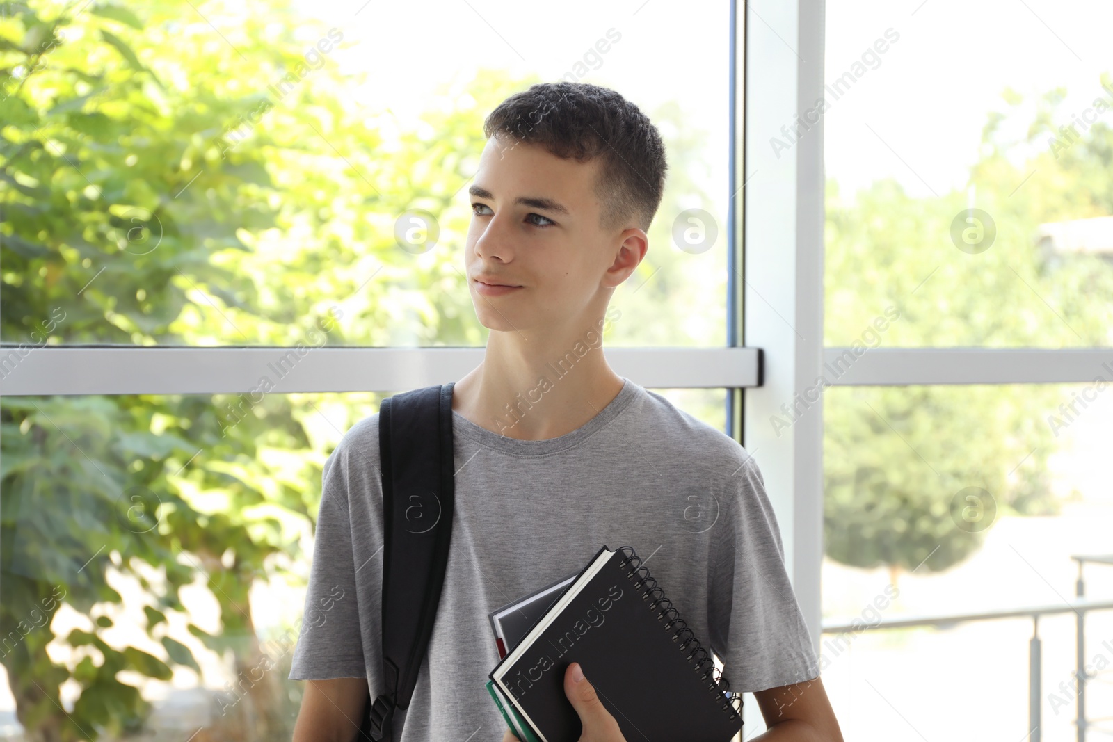 Photo of Portrait of teenage boy with backpack and books indoors