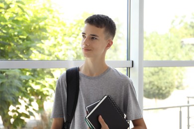 Portrait of teenage boy with backpack and books indoors