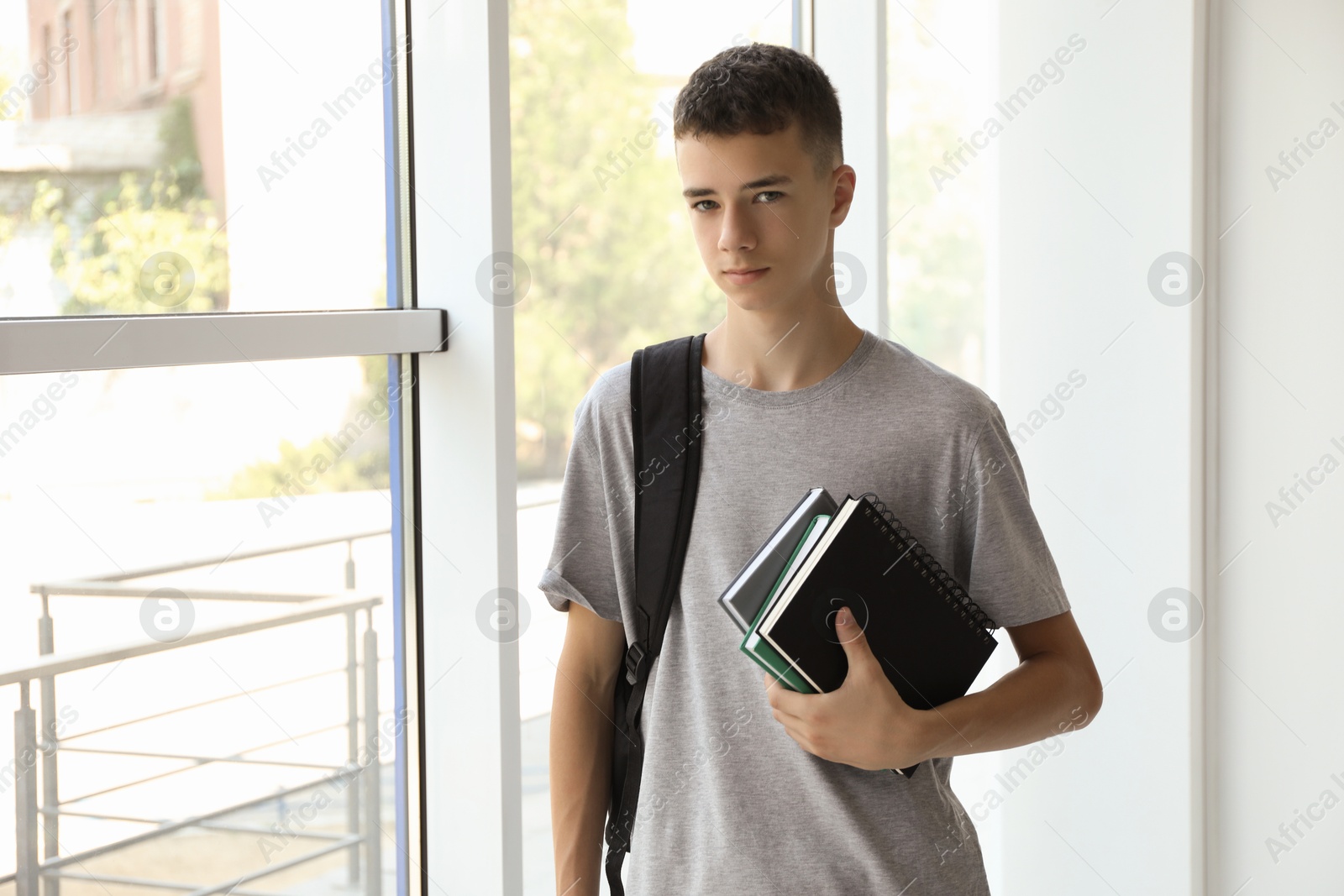 Photo of Portrait of teenage boy with backpack and books indoors