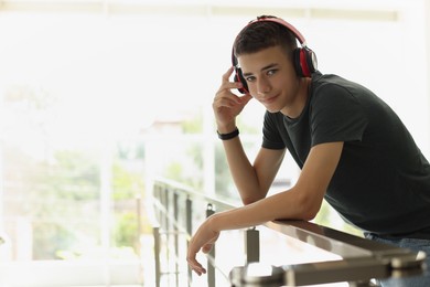 Photo of Portrait of teenage boy listening to music near railings indoors. Space for text