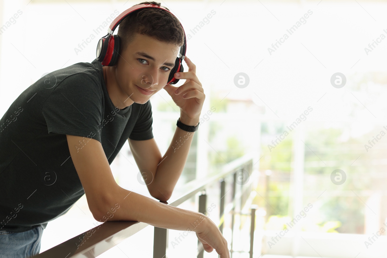 Photo of Portrait of teenage boy listening to music near railings indoors. Space for text