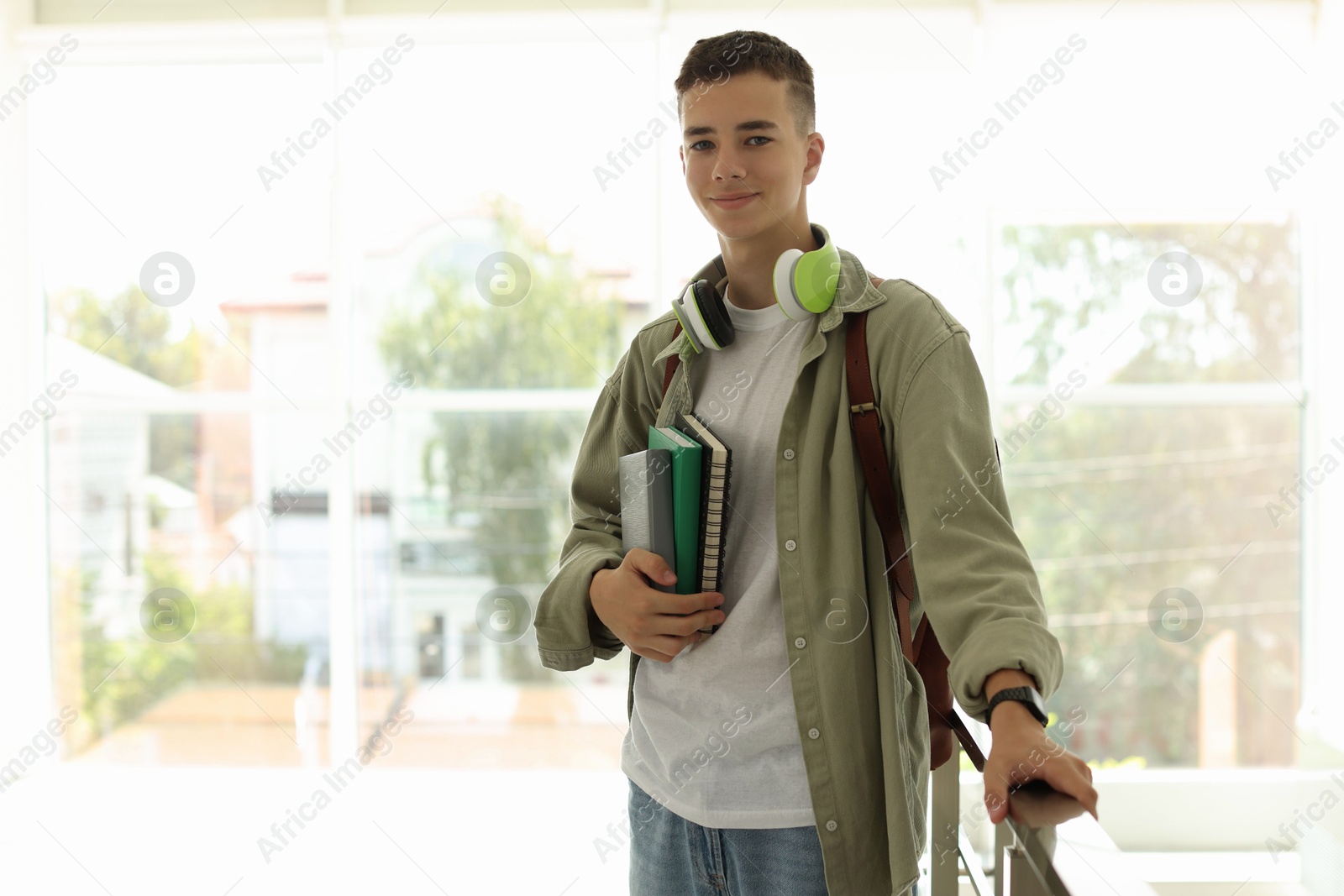 Photo of Portrait of teenage boy with books near railings indoors. Space for text