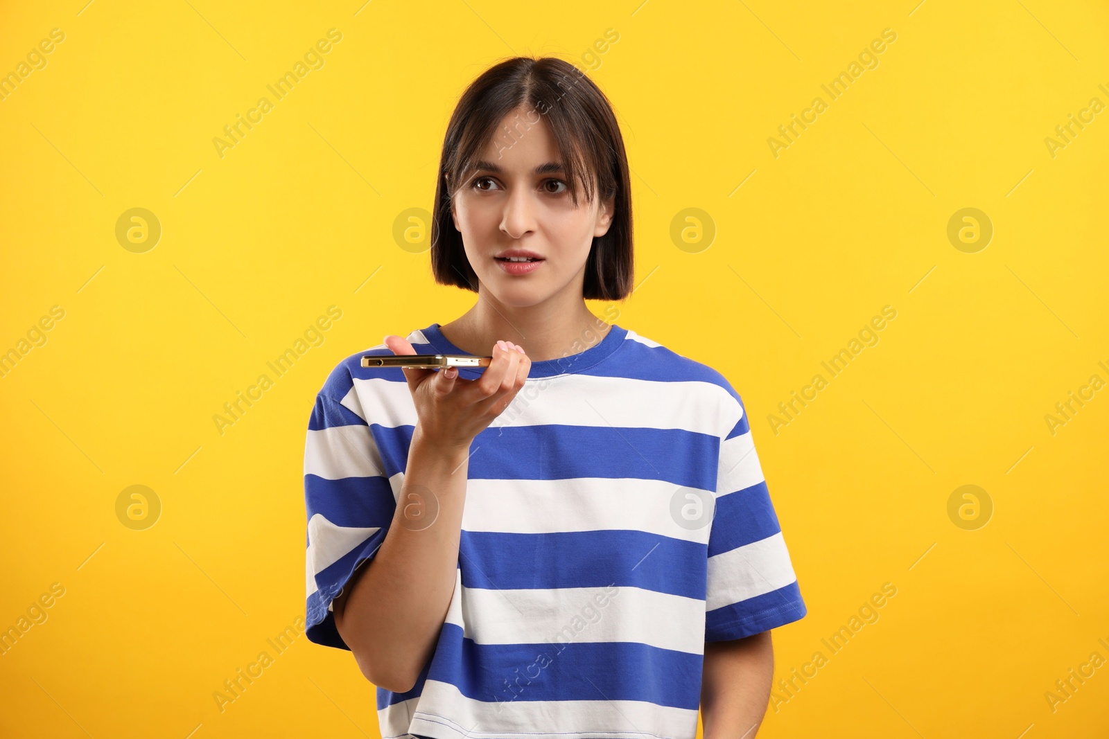 Photo of Beautiful woman recording voice message via smartphone on yellow background