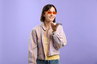 Photo of Beautiful woman recording voice message via smartphone on violet background