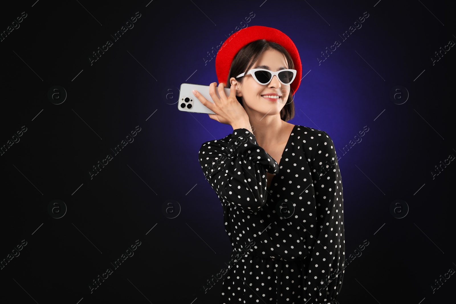 Photo of Stylish woman listening to voice message via smartphone on dark background, space for text