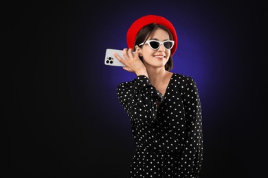 Photo of Stylish woman listening to voice message via smartphone on dark background, space for text