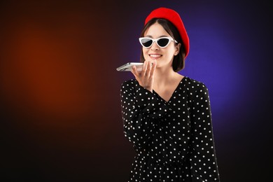 Stylish woman recording voice message via smartphone on color background, space for text