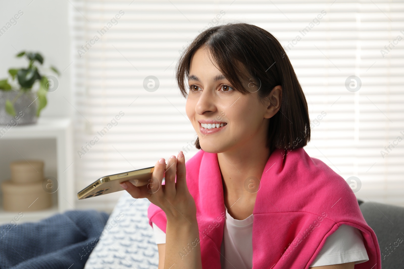 Photo of Beautiful woman recording voice message via smartphone at home