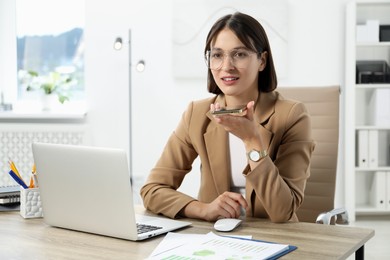 Photo of Beautiful woman recording voice message via smartphone in office